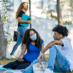 college students sitting on lawn with masks on