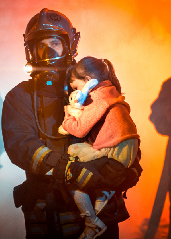 little girl being carried by firefighter away from active fire and flames in background