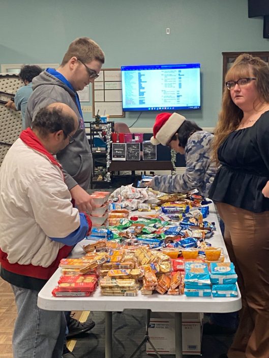 Three people standing around a long table with packaged snacks